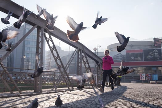 sporty woman running on sidewalk at early morning jogging with city  sunrise scene in background