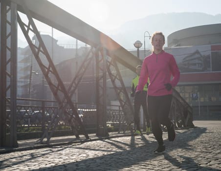 sporty woman running on sidewalk at early morning jogging with city  sunrise scene in background