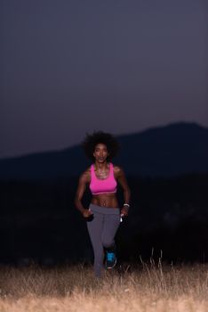 young African american woman runner with headphones jogging outdoors in nature beautiful summer night - Fitness, people and healthy lifestyle