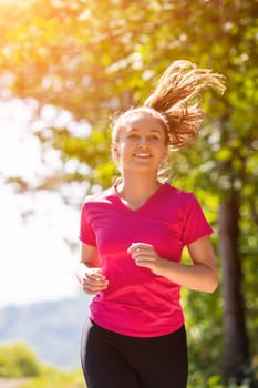 young happy woman enjoying in a healthy lifestyle while jogging on a country road through the beautiful sunny forest, exercise and fitness concept