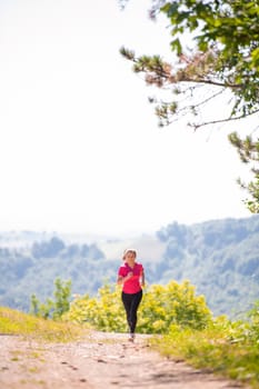 young happy woman enjoying in a healthy lifestyle while jogging on a country road through the beautiful sunny forest, exercise and fitness concept