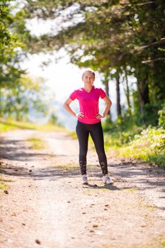 portyrait of young happy woman enjoying in a healthy lifestyle while jogging on a country road through the beautiful sunny forest, exercise and fitness concept