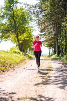 young happy woman enjoying in a healthy lifestyle while jogging on a country road through the beautiful sunny forest, exercise and fitness concept