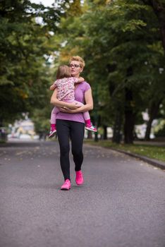 young sporty mother carries little daughter in arms while jogging in a city park,outdoor sports and fitness