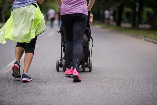 two young healthy women jogging together while pushing a baby stroller at city park