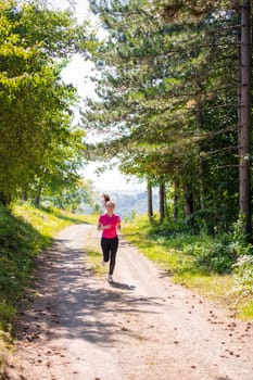 young happy woman enjoying in a healthy lifestyle while jogging on a country road through the beautiful sunny forest, exercise and fitness concept