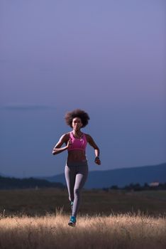 young African american woman runner with headphones jogging outdoors in nature beautiful summer night - Fitness, people and healthy lifestyle