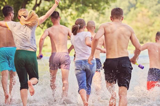 Summer joy group of happy friends having fun while running and splashing on river