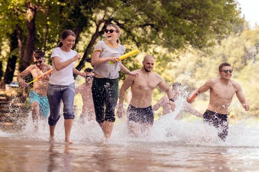 Summer joy group of happy friends having fun while running and splashing on river