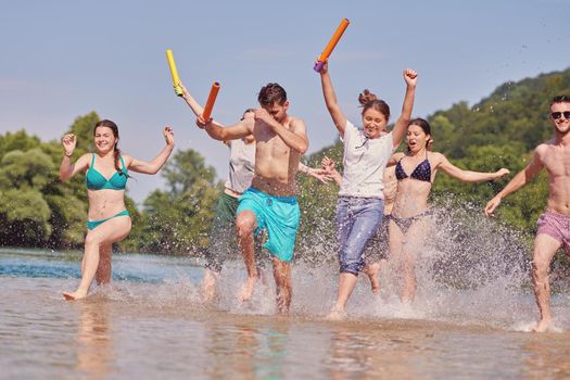 Summer joy group of happy friends having fun while running and splashing on river