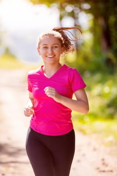 young happy woman enjoying in a healthy lifestyle while jogging on a country road through the beautiful sunny forest, exercise and fitness concept