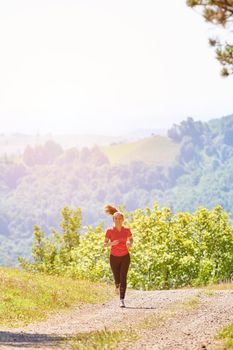 woman enjoying in a healthy lifestyle while jogging on a country road through the beautiful sunny forest, exercise and fitness concept