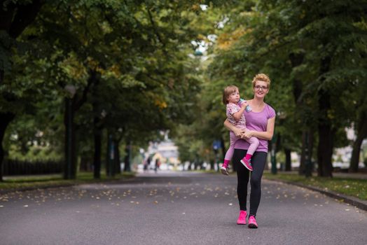 young sporty mother carries little daughter in arms while jogging in a city park,outdoor sports and fitness