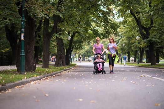 two young healthy women jogging together while pushing a baby stroller at city park