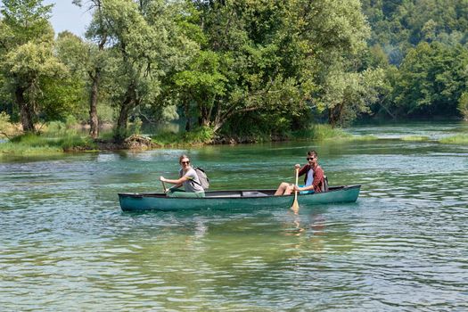 Couple adventurous explorer friends are canoeing in a wild river surrounded by the beautiful nature