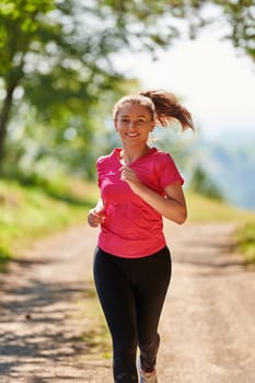 woman enjoying in a healthy lifestyle while jogging on a country road through the beautiful sunny forest, exercise and fitness concept