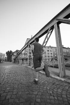 young sporty man jogging across the bridge at sunny morning in the city