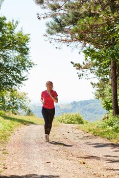 woman enjoying in a healthy lifestyle while jogging on a country road through the beautiful sunny forest, exercise and fitness concept