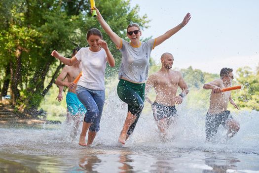 Summer joy group of happy friends having fun while running and splashing on river