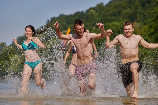 Summer joy group of happy friends having fun while running and splashing on river