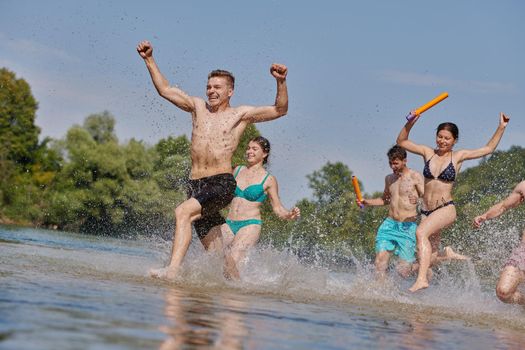 Summer joy group of happy friends having fun while running and splashing on river