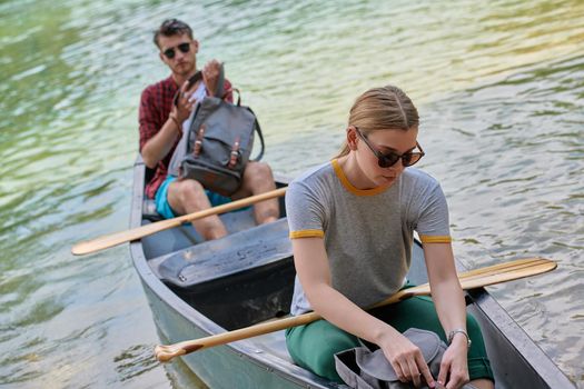 Couple adventurous explorer friends are canoeing in a wild river surrounded by the beautiful nature