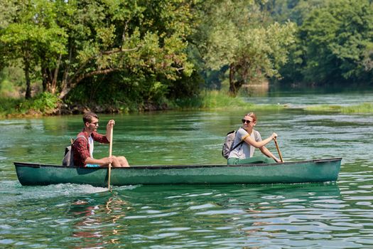 Couple adventurous explorer friends are canoeing in a wild river surrounded by the beautiful nature