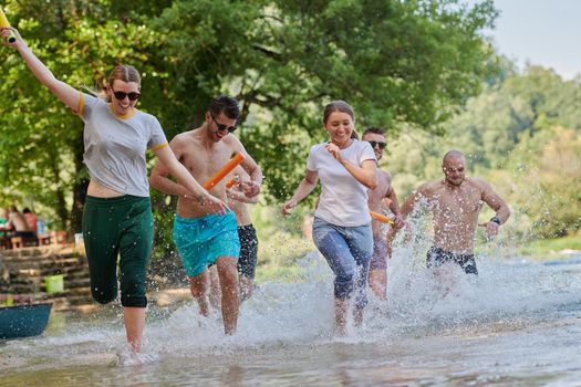 Summer joy group of happy friends having fun while running and splashing on river