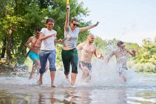 Summer joy group of happy friends having fun while running and splashing on river