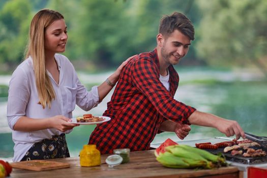 group of happy friends having picnic french dinner party outdoor during summer holiday vacation near the river at beautiful nature