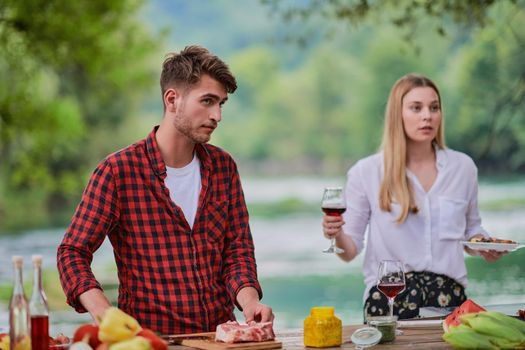 group of happy friends having picnic french dinner party outdoor during summer holiday vacation near the river at beautiful nature