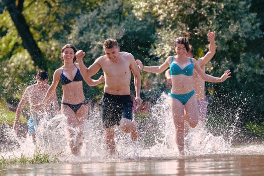 Summer joy group of happy friends having fun while running and splashing on river