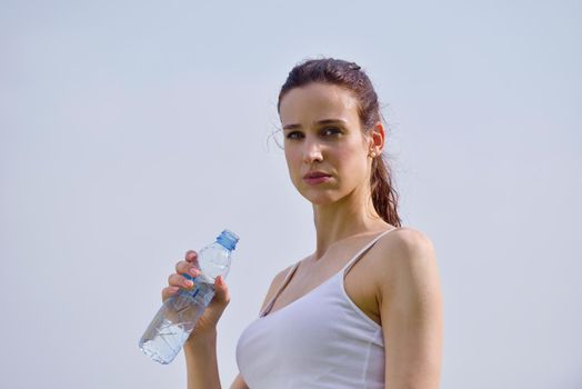 Young beautiful woman drinking water after fitness exercise and jogging outdoors