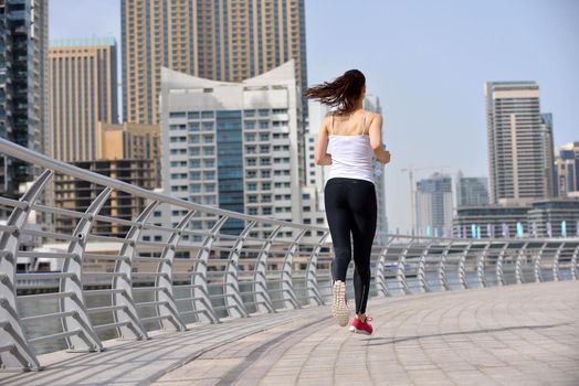 Running in city park. Woman runner outside jogging at morning with Dubai urban scene in background