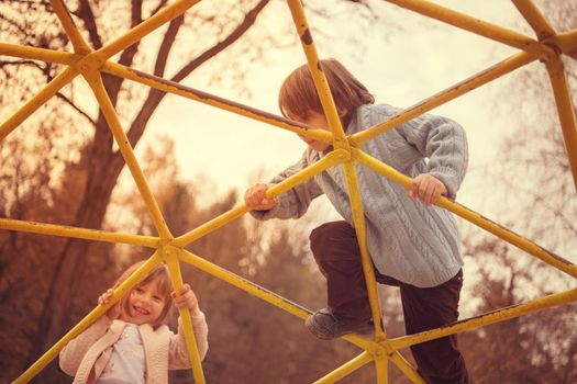 cutte little girl and boy in childrens park having fun and joy while playing in playground on autumn cloudy day