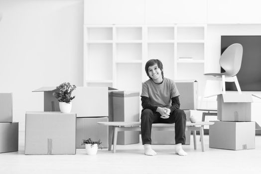 happy little boy sitting on the table with cardboard boxes around him in a new modern home