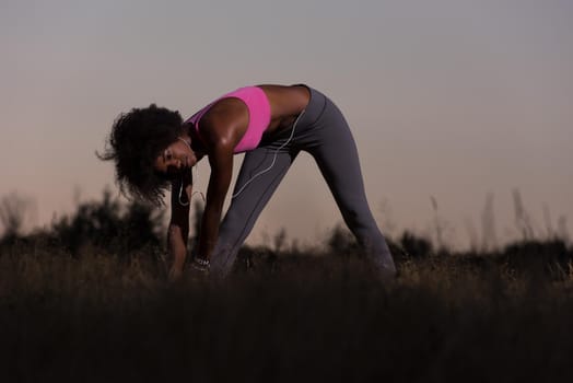 Young healthy black woman is doing stretching exercise relaxing and warm up after jogging and running in the nature beautiful summer evening