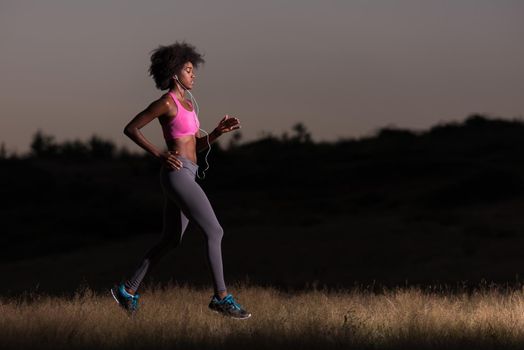 young African american woman runner with headphones jogging outdoors in nature beautiful summer night - Fitness, people and healthy lifestyle