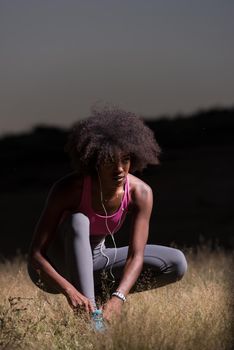 young African american woman runner tightening shoe lace in nature  Fitness, people and healthy lifestyle