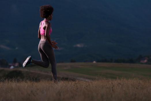 young African american woman runner with headphones jogging outdoors in nature beautiful summer night - Fitness, people and healthy lifestyle