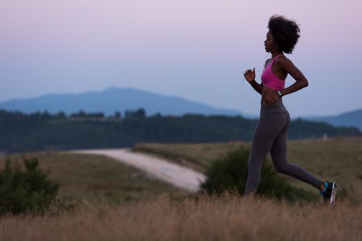 young African american woman runner with headphones jogging outdoors in nature beautiful summer night - Fitness, people and healthy lifestyle