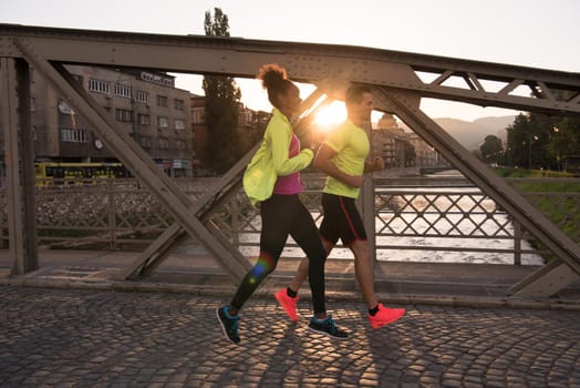 healthy young multiethnic couple jogging in the city at early morning with sunrise in background