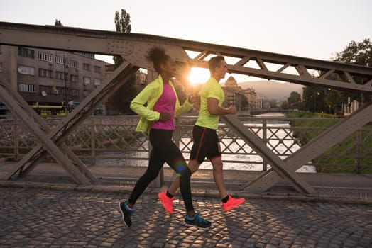 healthy young multiethnic couple jogging in the city at early morning with sunrise in background