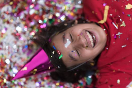 Happy kid celebrating party with blowing confetti while lying on the floor