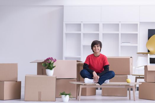 happy little boy sitting on the table with cardboard boxes around him in a new modern home