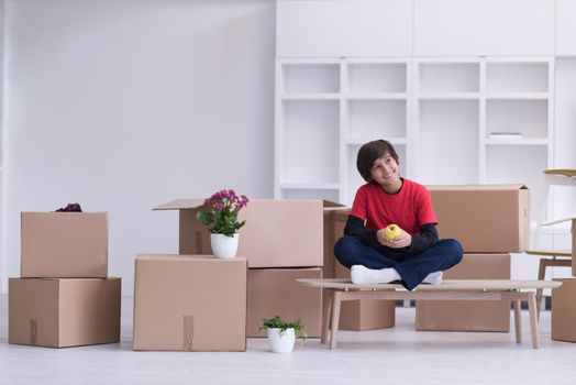 happy little boy sitting on the table with cardboard boxes around him in a new modern home