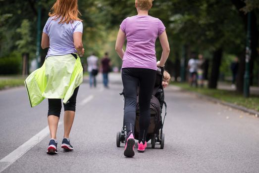 two young healthy women jogging together while pushing a baby stroller at city park