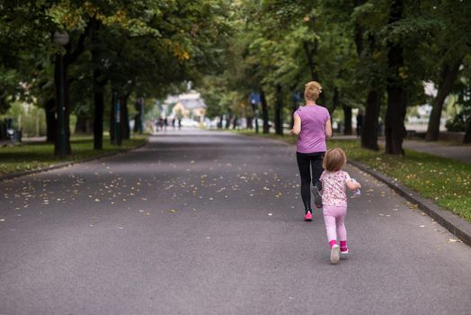 young sporty mother and little daughter jogging in a city park outdoor sports and fitness