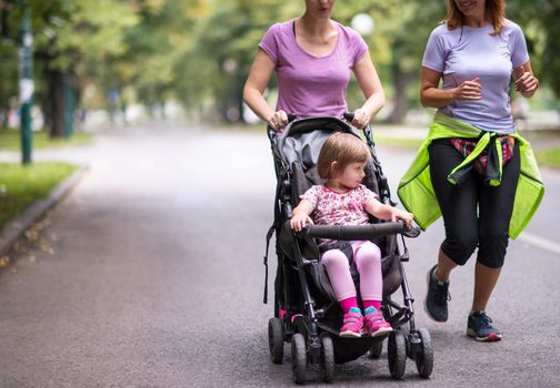 two young healthy women jogging together while pushing a baby stroller at city park