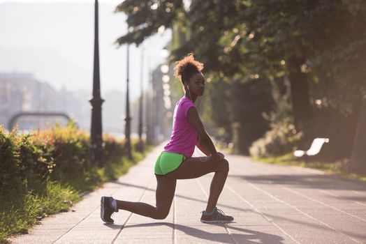 young beautiful African American woman doing warming up and stretching before the morning run with the sunrise in the background